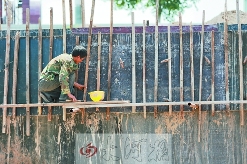 　　烈日下，狹窄的架子上，工人正用錘子固定樁基。