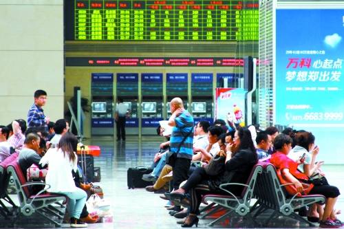 候車大廳溫度很高，一名乘客一手扇風(fēng)、一手擦汗