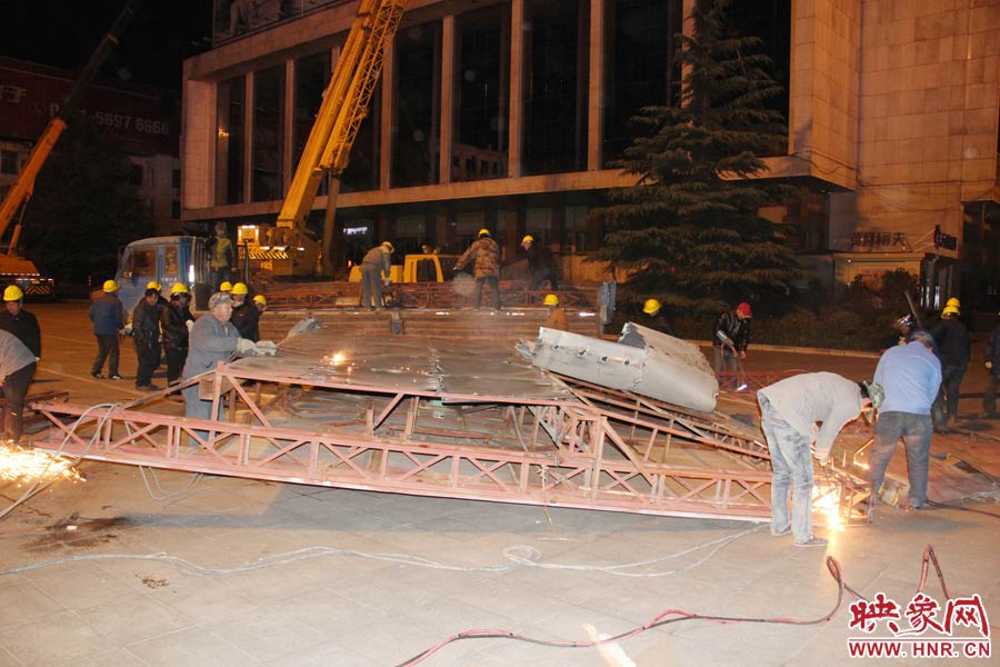 地面上的20多名工人對(duì)吊裝下的廣告牌進(jìn)行分割。