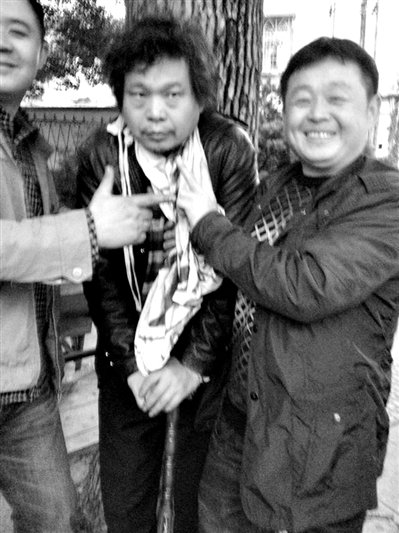 兩名接訪人員與患有癌癥的訪民段新德合影時(shí)，面帶笑容擺出勝利的手勢(shì)。