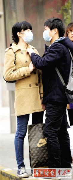 公交站臺(tái)上，一對(duì)年輕人戴著口罩，系緊衣領(lǐng)。